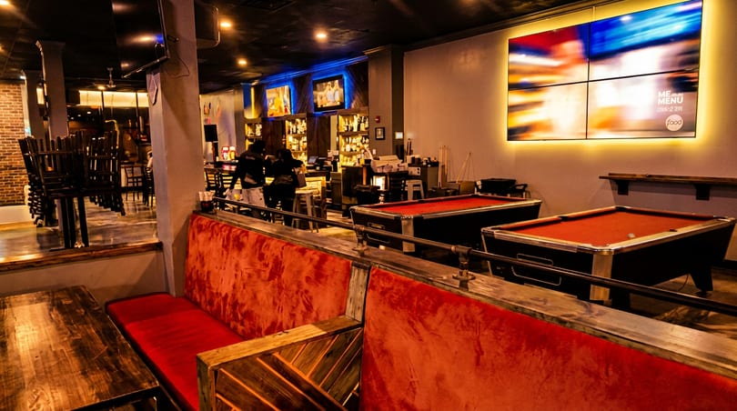 Restaurant interior with red velvet booths, two pool tables, a bar, and a large video wall.