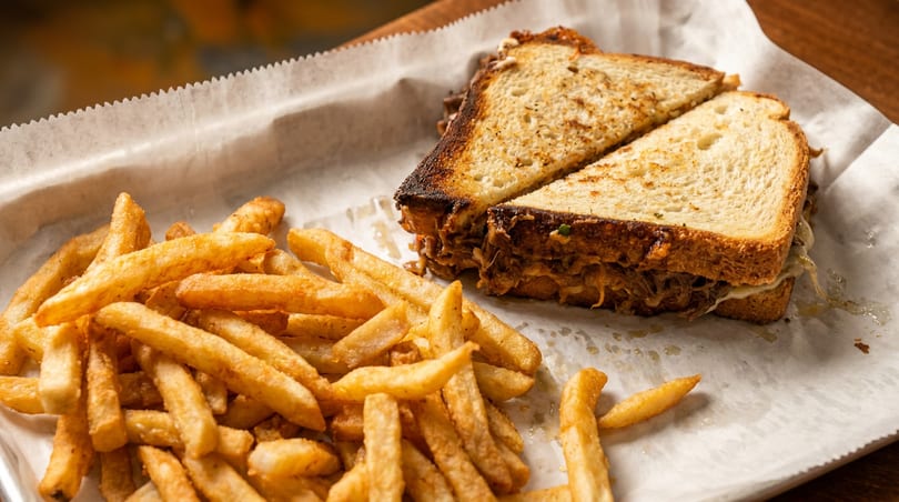 Pulled pork sandwich on toasted bread with a side of golden french fries on white paper.