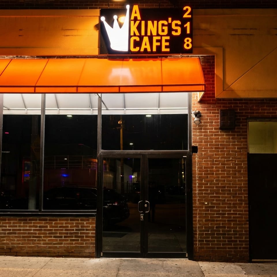 Exterior of A King's Cafe at night, with an orange awning and neon sign.